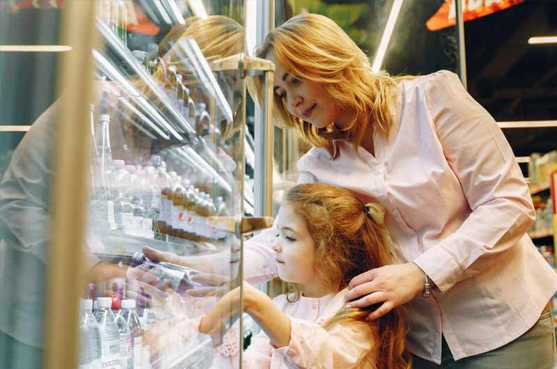 Madre-aiuta-la-figlia-a-prendere-bottiglia-dal-banco-frigo-di-un-supermercato-1
