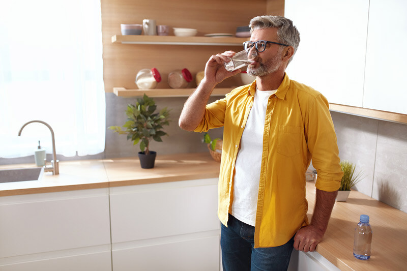 uomo-in-giallo-beve-bicchiere-dacqua-in-cucina